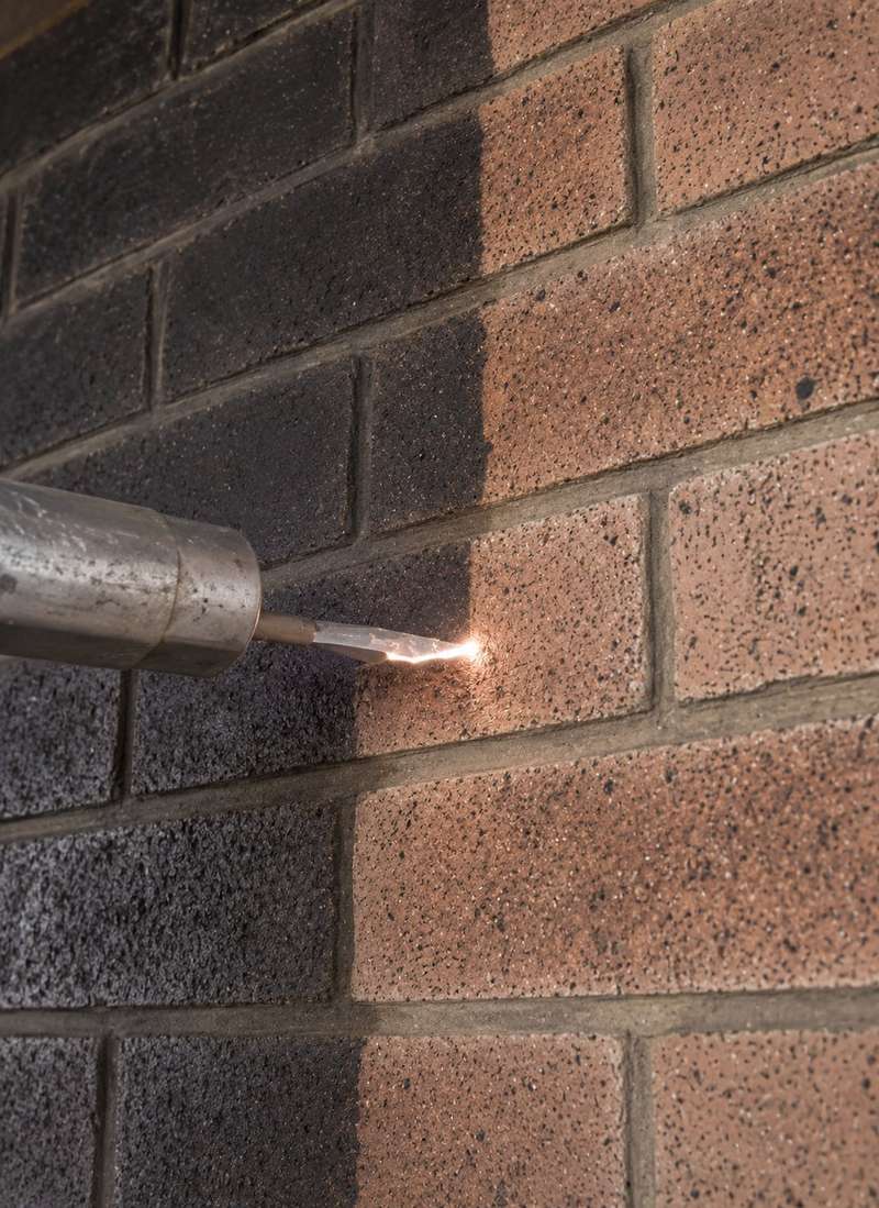 Laser soot removal in progress on a fire-damaged brick wall